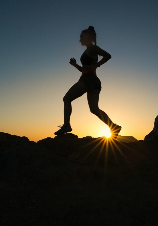 Silhouette of woman running with sunset behind her