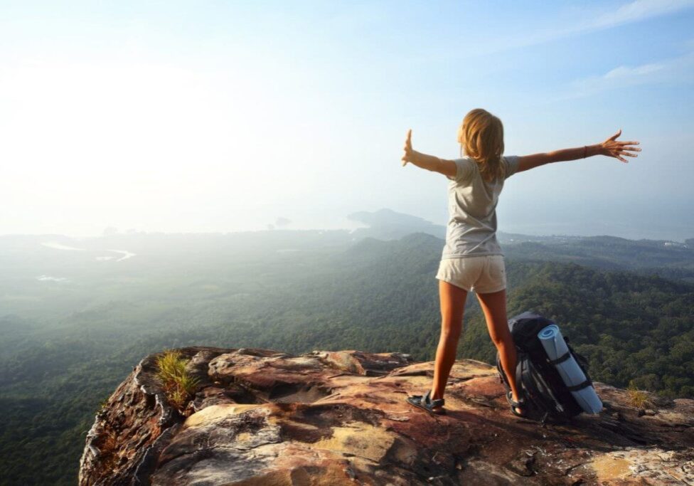 Woman at top of cliff with arms open overlooking mountain view