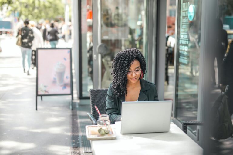 Woman sitting outside store at a table with laptop