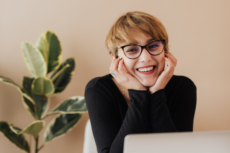 Woman leaning on table with hands under chin smiling